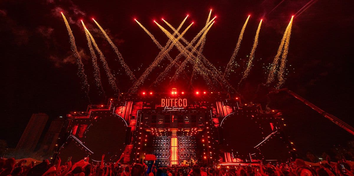 Palco do Buteco Para Sempre iluminado de vermelho, com fogos de artifício sobre o público