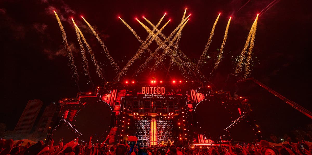 Palco do Buteco Para Sempre iluminado de vermelho, com fogos de artifício sobre o público